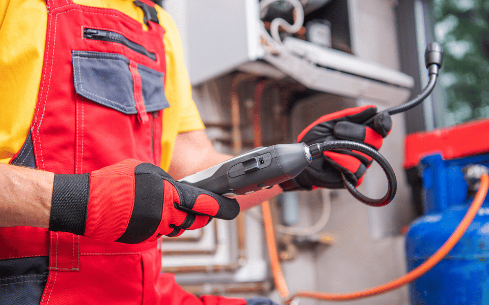Técnico con guantes y overol rojo utilizando un dispositivo especializado para detectar fugas de gas.